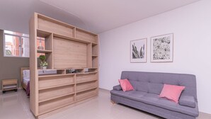 Un salon moderne avec un canapé gris, une étagère en bois et deux reproductions botaniques encadrées accrochées au mur.