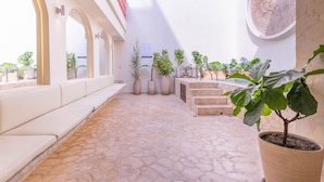 A sunlit courtyard with stone flooring, white seating, potted plants, and a staircase. - Casa Museo - Standar (Medellín)