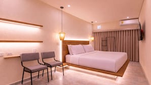 A hotel room with a bed, two chairs, a bedside table, a lamp, a window with curtains, and an air conditioning unit. - Casa Museo - Standar (Medellín)