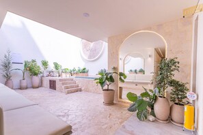 Un amplio espacio al aire libre con suelo de piedra, plantas en macetas, un área de estar y una piscina.