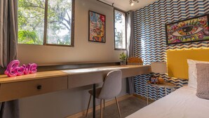 Een slaapkamer met een bed, een bureau en een stoel. Er zijn twee ramen, waarvan er één gordijnen heeft en de ander niet.