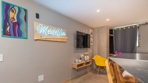 Een moderne kamer met een neonbord, een televisie, een houten plank met decoratieve objecten, een gele stoel en een metalen tafel.