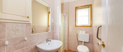 A bathroom with a sink, toilet, shower, and a window.