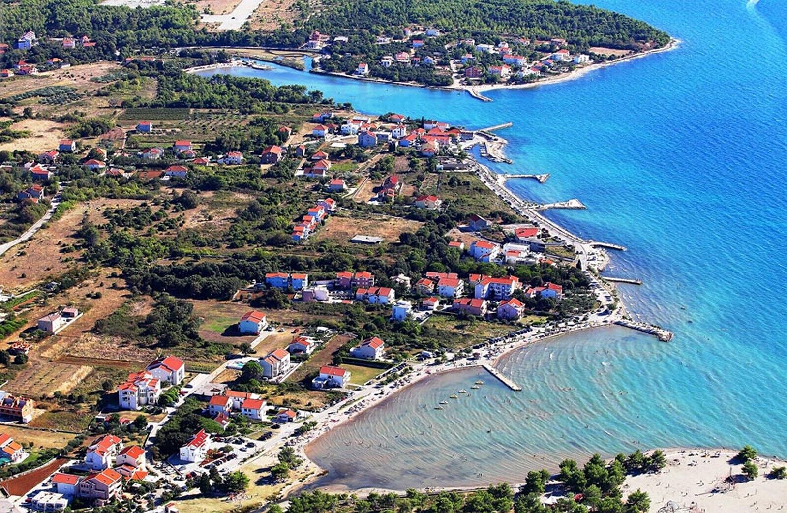 Une vue aérienne d’une ville côtière avec des maisons, une plage et une jetée.