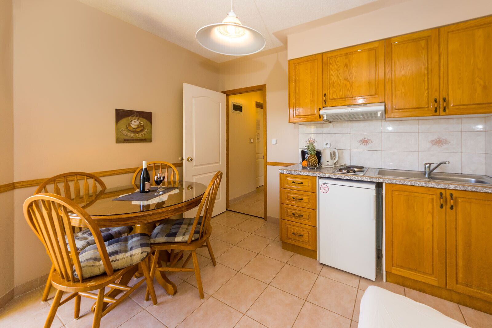 Cocina compacta con armarios de madera, una pequeña encimera y un comedor con una mesa redonda y sillas.