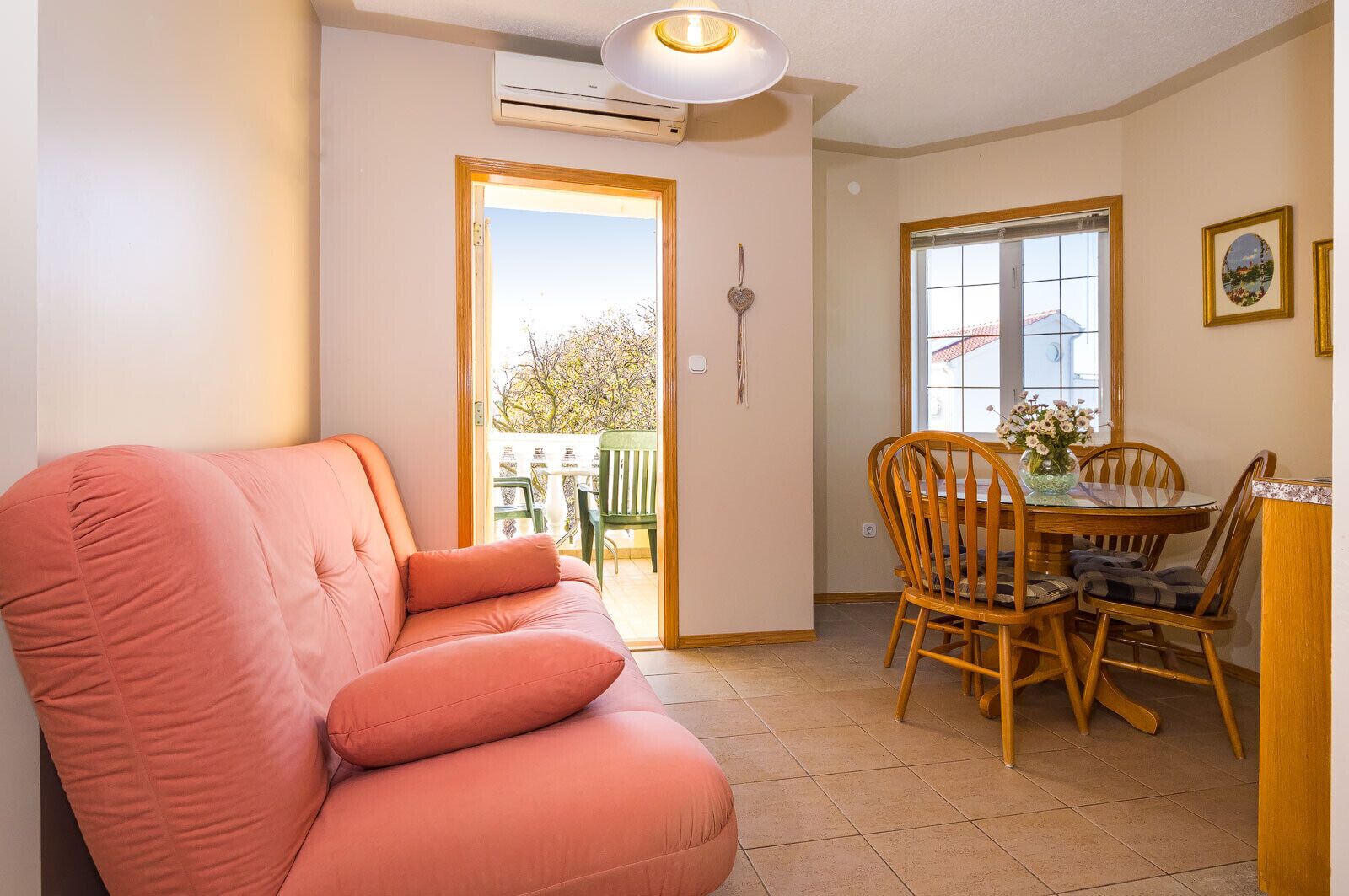 Une pièce avec un canapé rose, une table à manger avec des chaises, une fenêtre donnant sur un beau paysage et un appareil de climatisation.