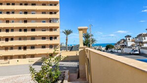 Hotel de varios pisos con balcones, una palmera y una vista despejada del mar.