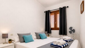 Una cama bien hecha con una colcha gris, dos almohadas y toallas enrolladas.