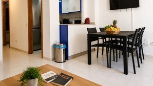 Una cocina moderna con un reloj, una mesa de comedor con sillas, un televisor montado en la pared y un cubo de basura.