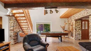 A cozy living room with a stone wall, a wooden ceiling, a leather armchair, a pool table, and a wooden bench. - Grand Le Jeanneau Cottage with Spa, Peaceful Nature Retreat for 15 Guests (Vallons-de-l'Erdre)