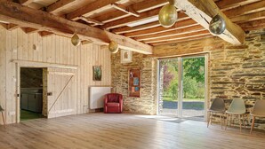 A spacious room with wooden floors, a stone wall, a red chair, and a large sliding glass door leading to an outdoor area. - Grand Le Jeanneau Cottage with Spa, Peaceful Nature Retreat for 15 Guests (Vallons-de-l'Erdre)