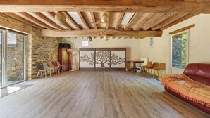 A spacious room with a stone wall, wooden beams, a large tree mural, and a red leather sofa. - Grand Le Jeanneau Cottage with Spa, Peaceful Nature Retreat for 15 Guests (Vallons-de-l'Erdre)