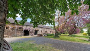 A stone building with a gravel driveway and a tree with purple flowers. - Grand Le Jeanneau Cottage with Spa, Peaceful Nature Retreat for 15 Guests (Vallons-de-l'Erdre)
