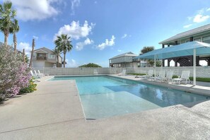 A swimming pool with lounge chairs, palm trees, and a covered seating area. - Lasting Respite – Coastal Getaway w/ Pond Views, Pool & Beach Access (Port Aransas)