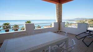Un'area esterna coperta con tavolo e sedie, un pilastro in pietra e vista sul mare.