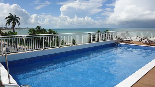 A swimming pool with a view of the ocean, a white railing, and lounge chairs. - Jardins do Atlântico - Miramar  (João Pessoa)