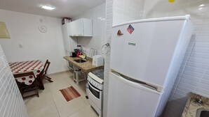 A kitchen with white cabinets, a refrigerator, a stove, and a dining table with chairs. - Jardins do Atlântico - Miramar  (João Pessoa)