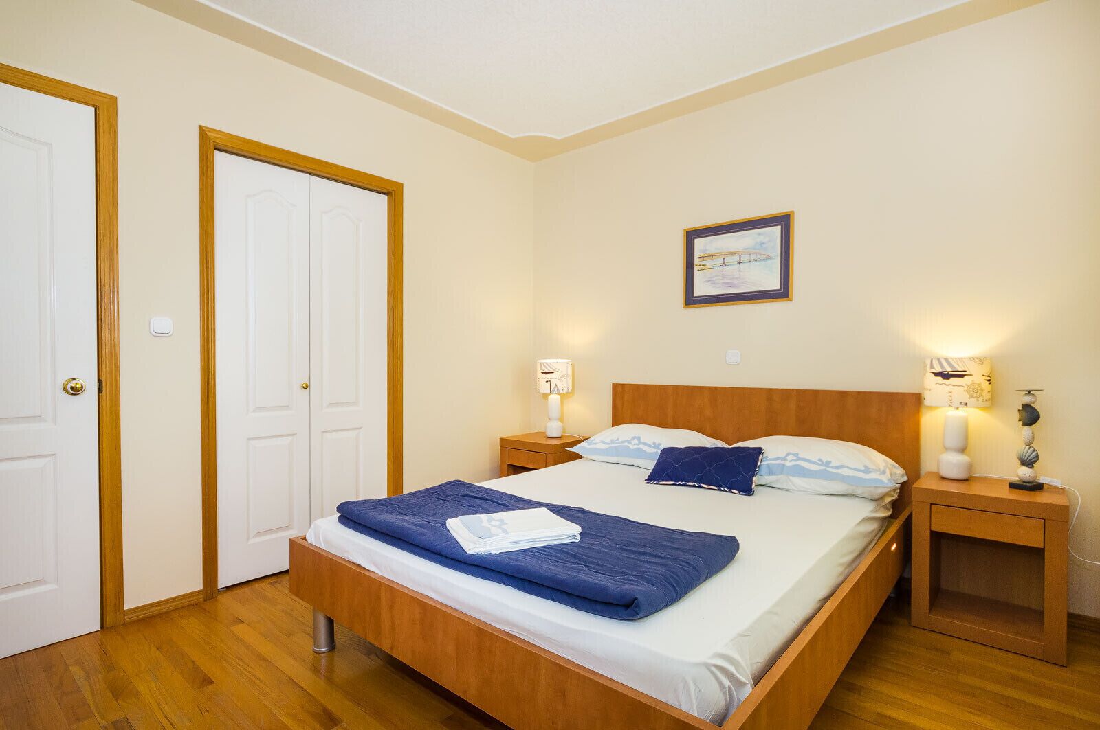 A bedroom with a wooden bed, two nightstands, a framed picture on the wall, and a door.