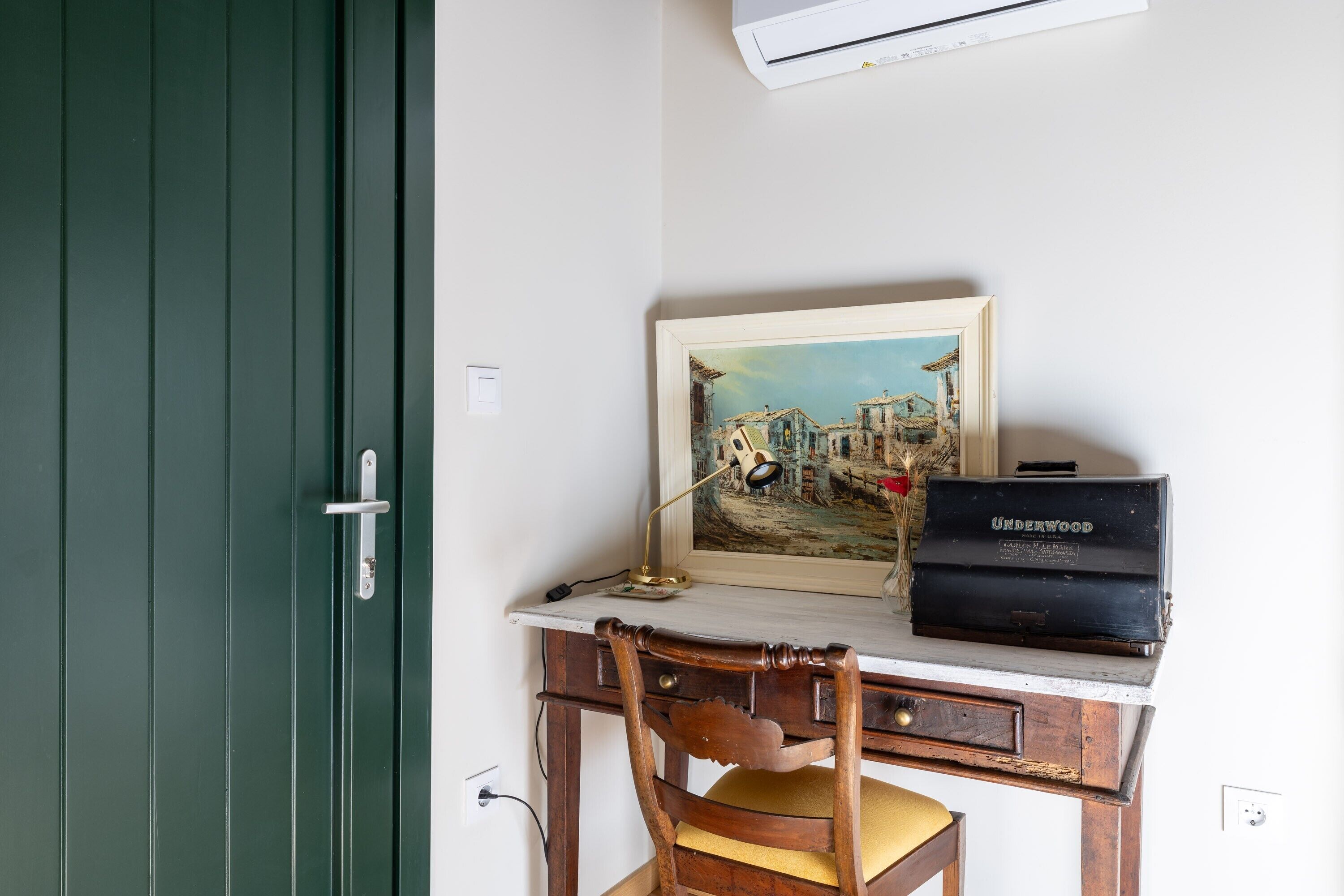 A desk with a framed painting, a lamp, and a vintage Underwood typewriter.