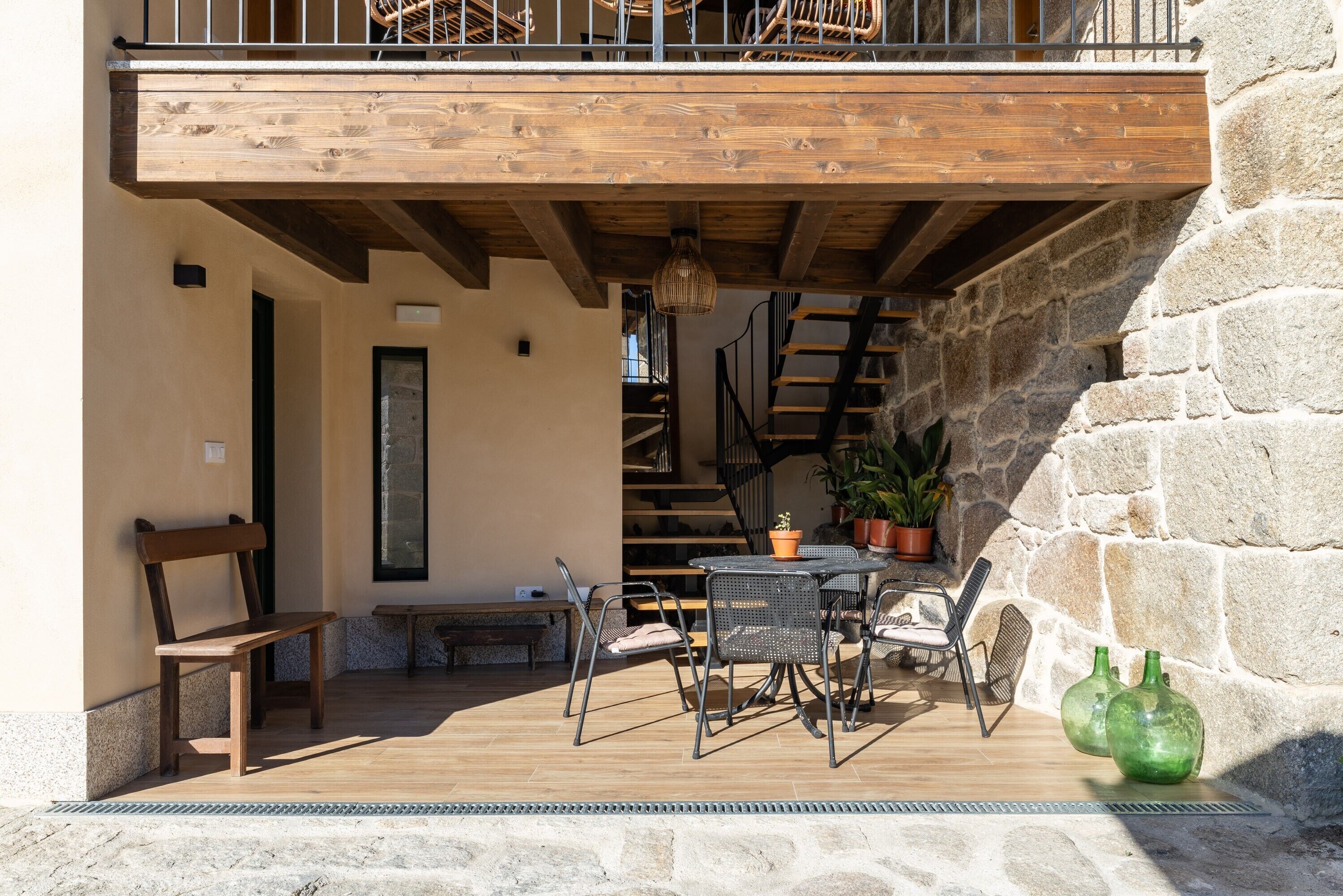 A wooden deck with outdoor furniture, a staircase, and stone walls.