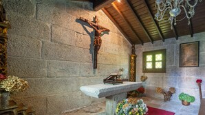 Un muro de piedra con una cruz, un banco de madera y una araña.