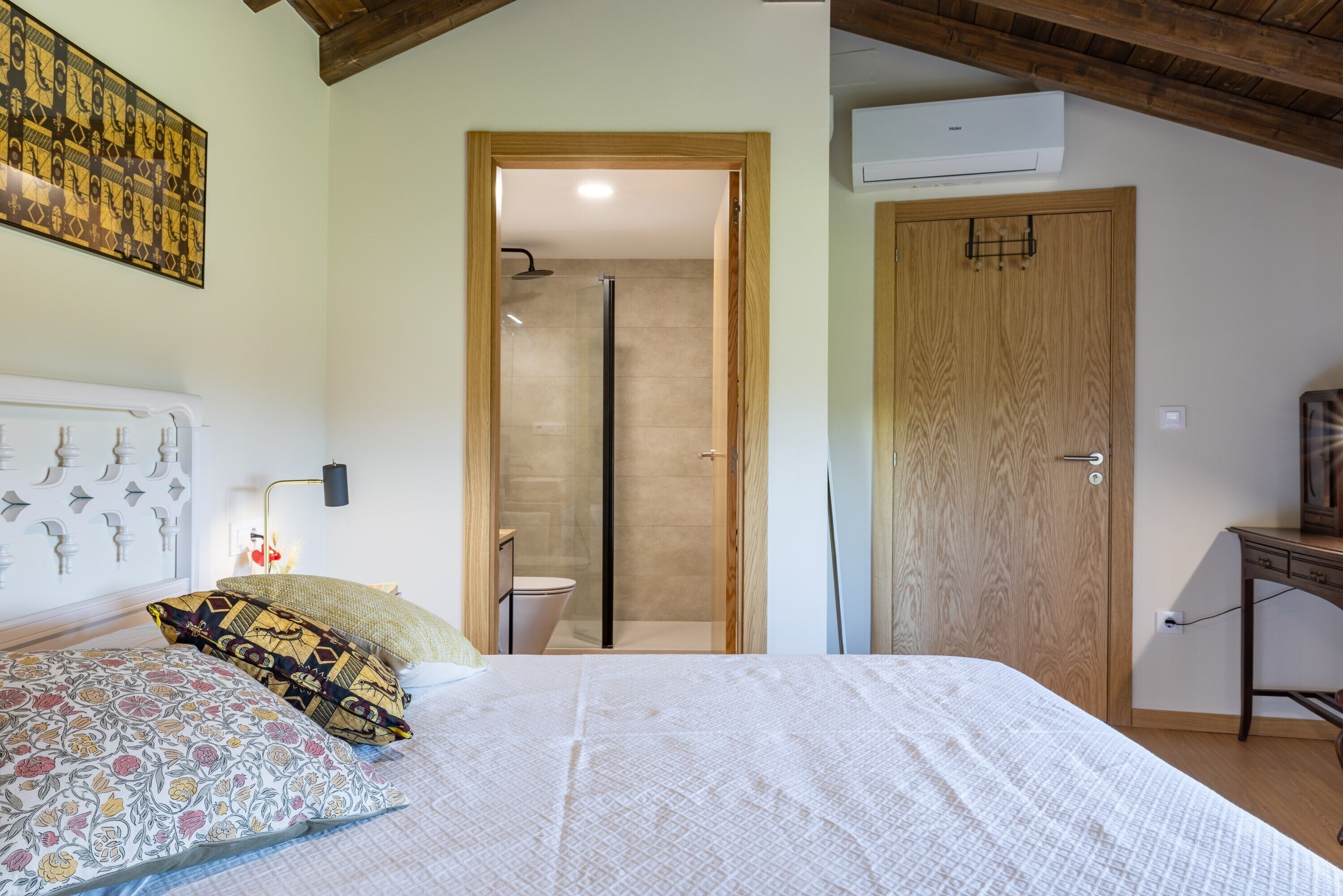 A bedroom with a bed, a wooden door, a shower, and a wall-mounted air conditioner.