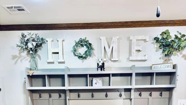 A room with a grey bench, a wall-mounted coat rack, and a 'HOME' sign above.
