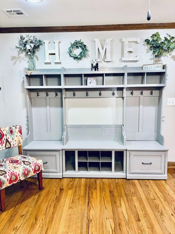 A room with a grey bench, a wall-mounted coat rack, and a 'HOME' sign above.