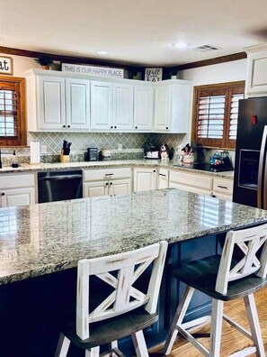 A kitchen with white cabinets, a granite countertop, and a bar area with stools. - Park Place-Where the Stars Stay! (Pawhuska)