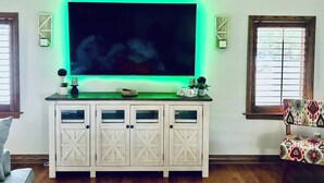 A living room with a large flat-screen TV, a white cabinet with glass doors, and a patterned chair.