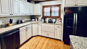 A kitchen with white cabinets, a black refrigerator, and a window with blinds.