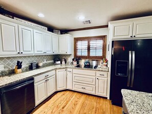 A kitchen with white cabinets, a black refrigerator, and a window with blinds.