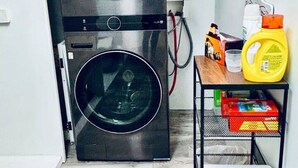 A compact laundry room with a double-door LG washer and dryer, a metal shelf with cleaning supplies, and a wooden floor.