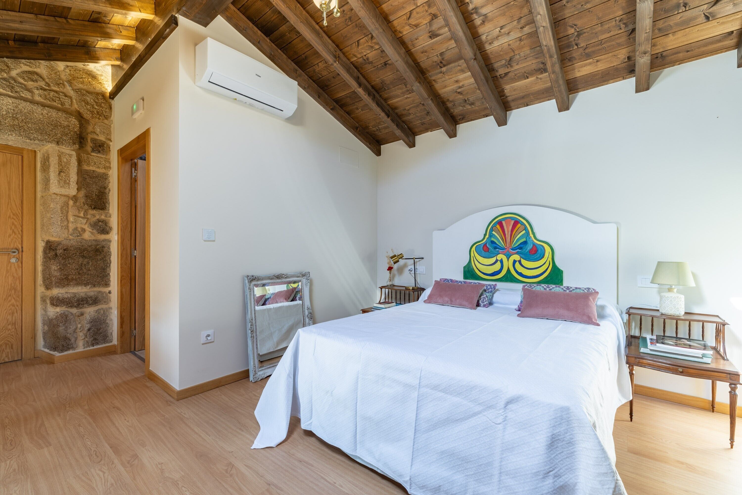 Ein Schlafzimmer mit Holzbalkendecke, einem Bett mit weißer Bettwäsche, einer Steinwand und einem Spiegel.