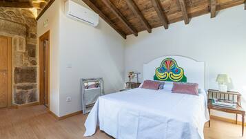 Ein Schlafzimmer mit Holzbalkendecke, einem Bett mit weißer Bettwäsche, einer Steinwand und einem Spiegel.