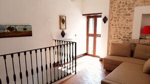 Una habitación con piso de madera, un sofá color beige, baranda de metal negro, una puerta de madera y un aplique de pared.