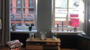 A room with a large window, a radiator, a small table with decorative items, and a patterned rug. - Godewind 1 Apartments with Wi-Fi (Jever)