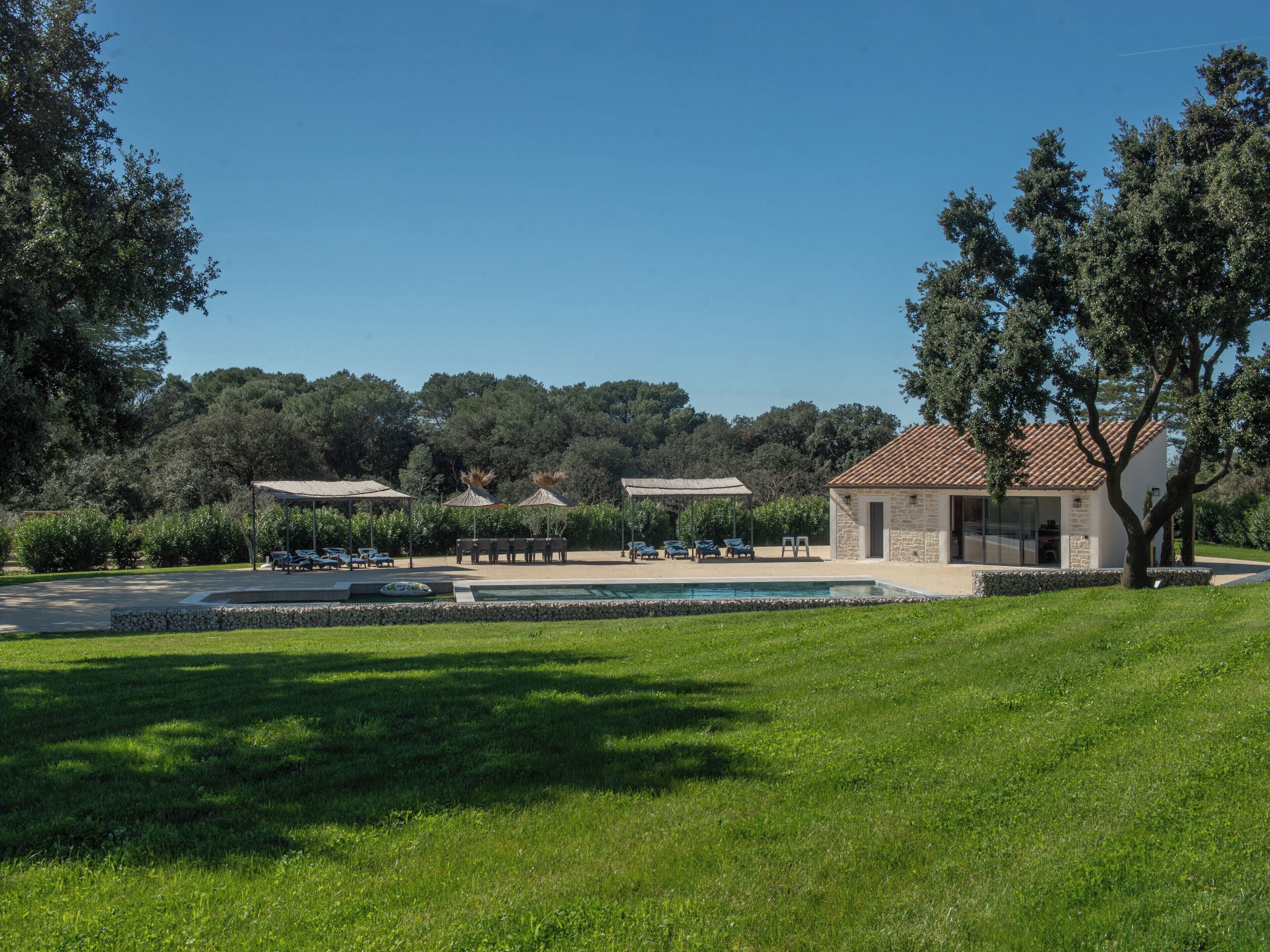 Un espace piscine avec des chaises longues, un bâtiment en pierre et un ciel d’un bleu limpide.
