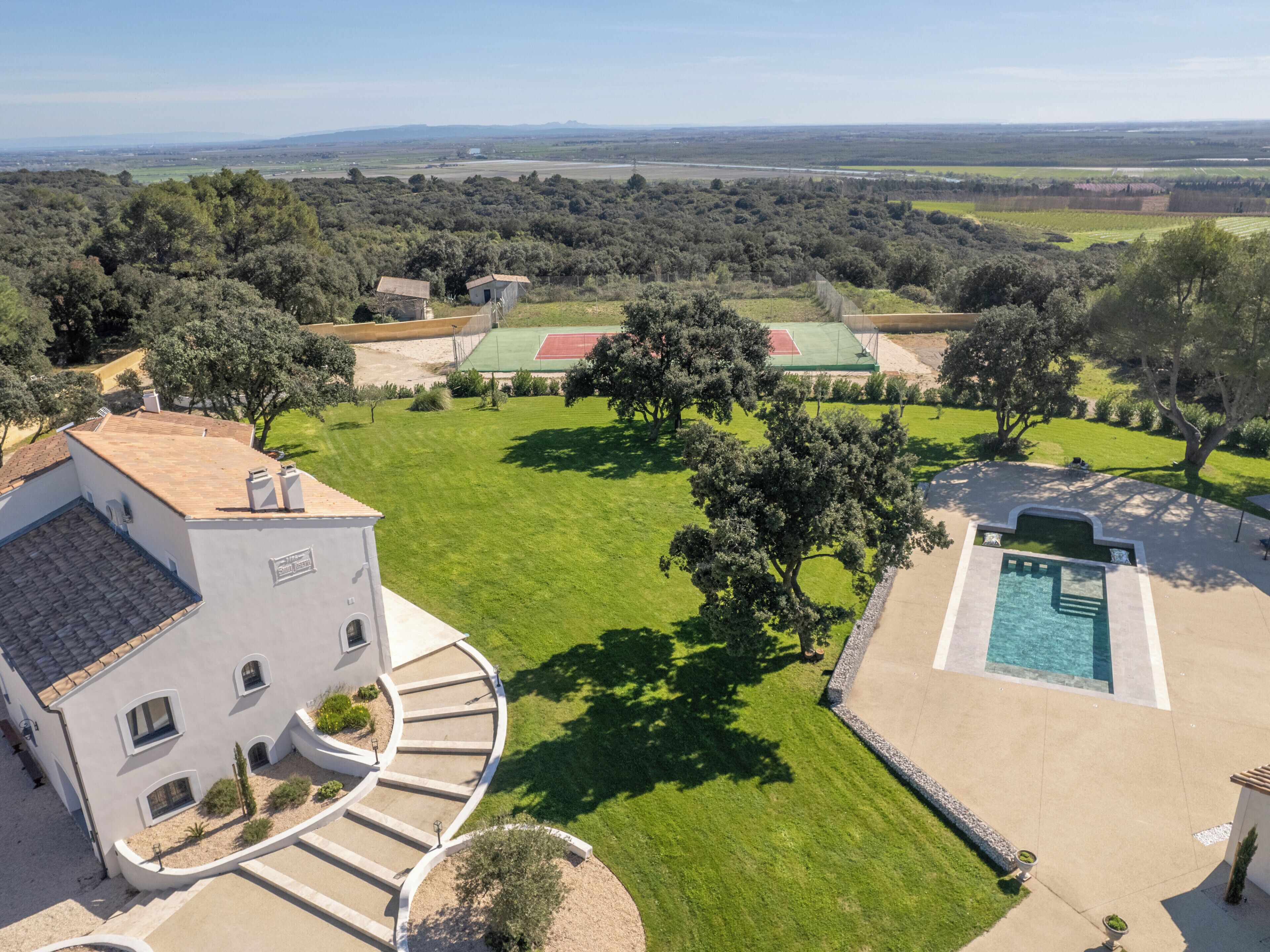 A large house with a swimming pool, a tennis court, and a well-maintained lawn.
