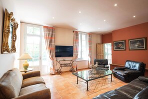 A living room with a TV, leather sofas, a glass coffee table, and a fireplace.