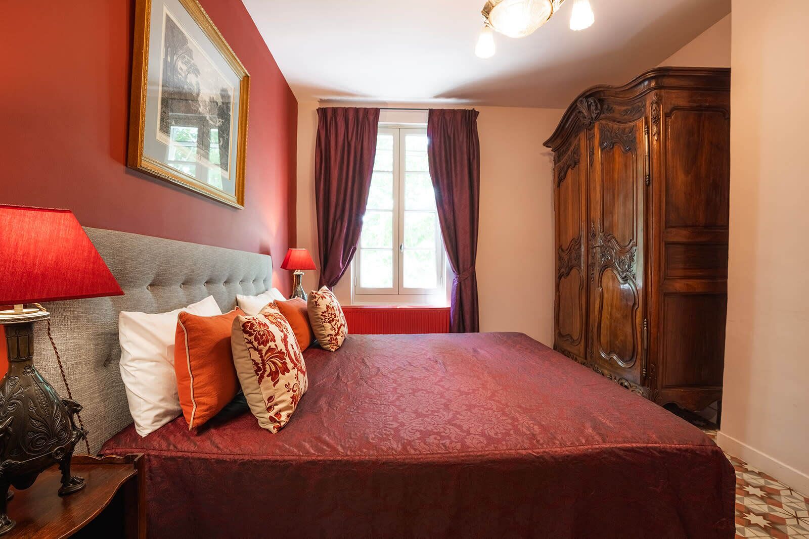 Een slaapkamer met een groot bed, een houten garderobe, een rode lamp en een ingelijst schilderij aan de muur.