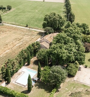 An aerial view of a property with a swimming pool, surrounded by dense trees and a large field.