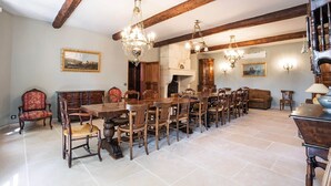 Une salle à manger avec une longue table en bois, de nombreuses chaises et des lustres décoratifs.