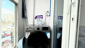 A laundry room with a washing machine, a mop, and a package of Boost detergent. - SKYHOME 2 GIUONG DOI A9 (Ho Chi Minh City)