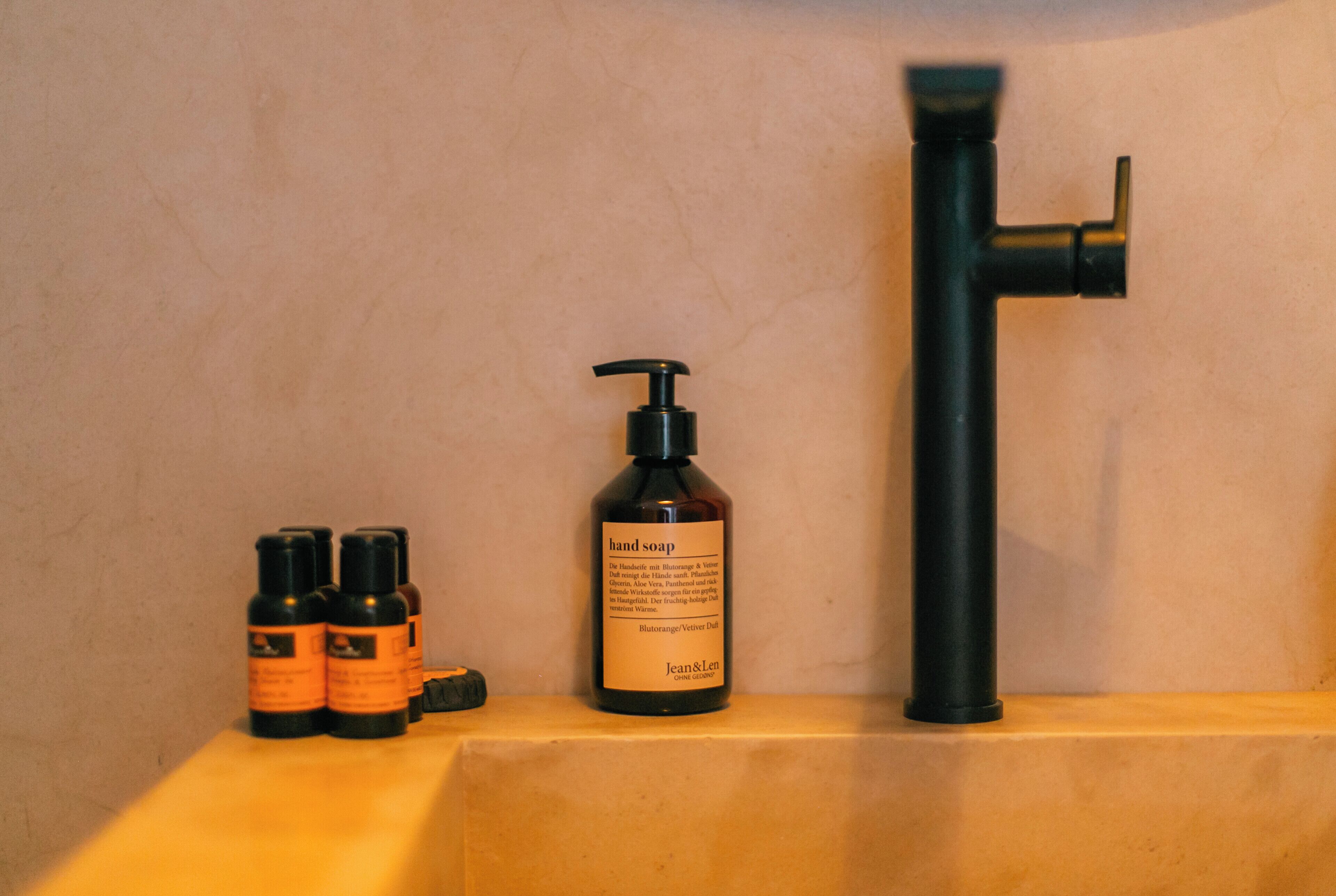 A bathroom with a hand soap bottle, a faucet, and two smaller bottles.
