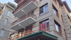 A multi-story building with balconies, a green overhang, and a visible entrance. - Hotel The Red Apple  (Manali)