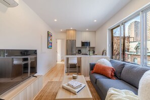 A modern apartment with a kitchen, dining area, and a living room with a sofa and a large window. - Chic Urban Escape – 2BR Retreat Montreal Living (Montréal)