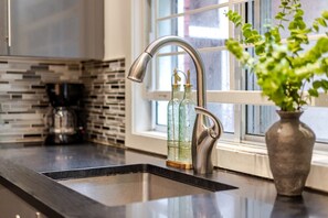A modern kitchen with a stainless steel faucet, a black countertop, and a window with a view. - Grand Urban Retreat – Spacious 5BR Heart MTL (Montréal)