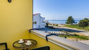 Uma varanda com parede amarela, uma mesa com xícaras e vista para a praia e edifícios.