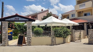 A building with a stone entrance, outdoor umbrellas, and a signboard. - Beachfront Apartment Mareo 4 (Nin)
